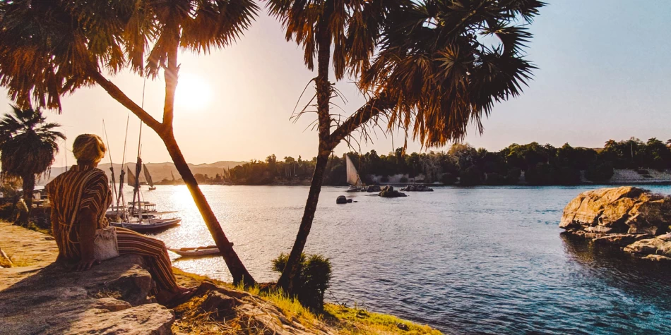 Sunset over the Nile River in Aswan framed by trees.